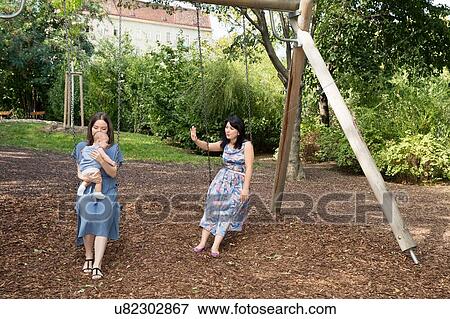 Stock Photo - Young woman with mother and baby daughter sitting on swings in park. Fotosearch