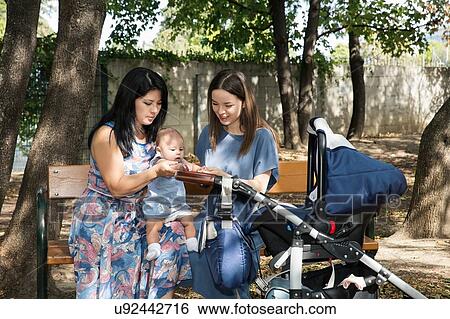 Stock Photograph - Young woman with mother and baby daughter sitting on park bench. Fotosearch
