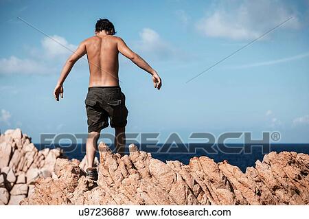 Stock Photo - Bare chested young man wearing khaki shorts climbing over rocks, Costa Smeralda, Sardinia, Italy. Fotosearch