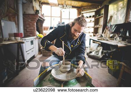 Bearded mid adult man in workshop sitting at pottery wheel using diddler to make clay pot View Large Photo Image Stock Photo - Bearded mid adult man in workshop sitting at pottery wheel using diddler to make clay pot. Fotosearch