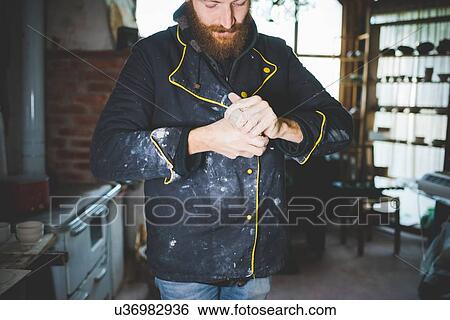 Bearded mid adult man squeezing clay in hands, looking down View Large Photo Image Stock Photograph - Bearded mid adult man squeezing clay in hands, looking down. Fotosearch