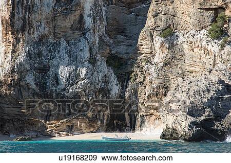 Boat on water by cave in cliff, Golfo di Orosei, Sardinia, Italy View Large Photo Image Stock Photo - Boat on water by cave in cliff, Golfo di Orosei, Sardinia, Italy. Fotosearch