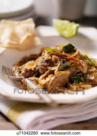 Stock Image - Bowl of black lamb curry with onions, lime slice and papadums. Fotosearch