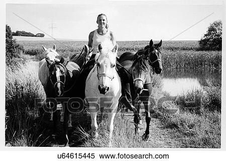 Stock Photography - B&W image of woman riding and leading six horses on dirt track. Fotosearch