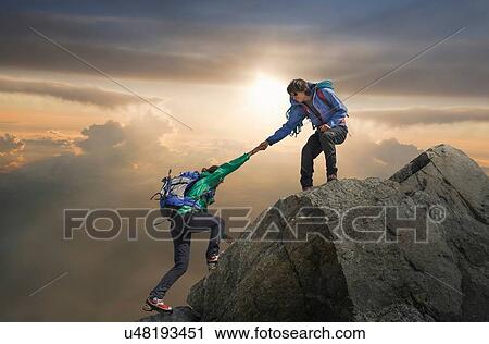 Stock Image - Climber helping partner reach mountain top, Mont Blanc, France. Fotosearch
