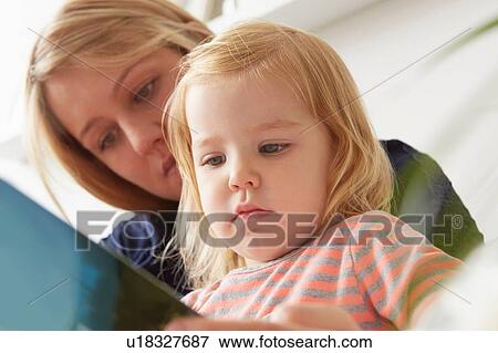 Stock Photo - Close up of woman and toddler daughter reading book. Fotosearch