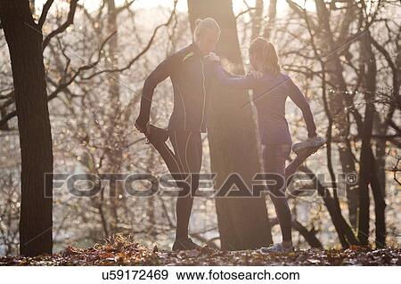 Stock Photo - Couple in forest leaning against each other leg raised holding foot stretching. Fotosearch