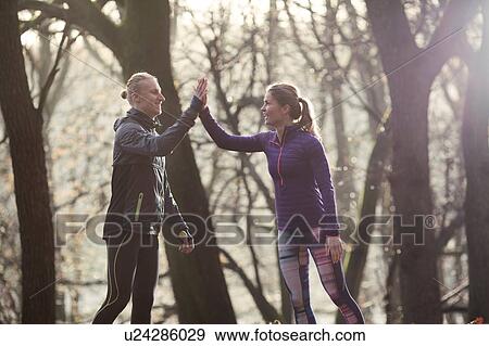 Stock Photo - Couple in forest wearing sport clothing doing high five smiling. Fotosearch