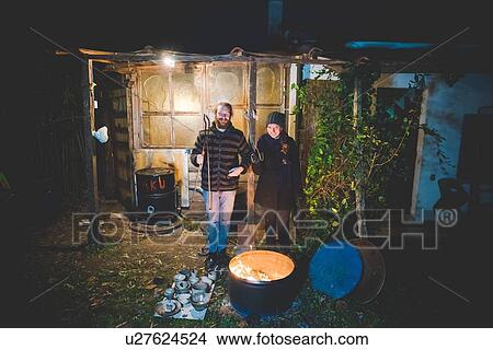 Picture - Couple in front of shed holding tongs, with pottery by fire in barrel. Fotosearch