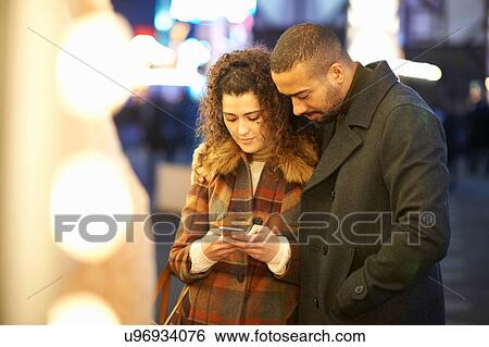 Couple looking at smartphone, outdoors, at night View Large Photo Image Stock Photograph - Couple looking at smartphone, outdoors, at night. Fotosearch