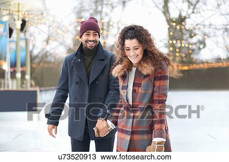 Stock Image - Couple on ice rink holding hands smiling. Fotosearch