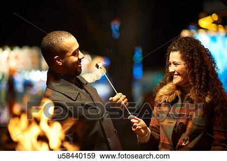 Couple outdoors, at night, woman feeding man toasted marshmellow View Large Photo Image Stock Photo - Couple outdoors, at night, woman feeding man toasted marshmellow. Fotosearch