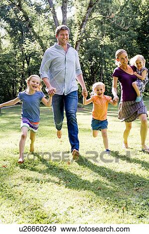 Couple running and holding hands with three daughters in park View Large Photo Image Stock Photo - Couple running and holding hands with three daughters in park. Fotosearch