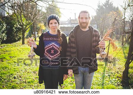 Couple standing in garden holding fresh garlic bulbs looking at camera smiling View Large Photo Image Stock Image - Couple standing in garden holding fresh garlic bulbs looking at camera smiling. Fotosearch