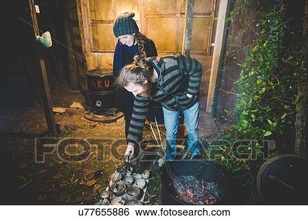 Stock Photograph - Couple using tongs to remove clay pots from fire, smiling. Fotosearch