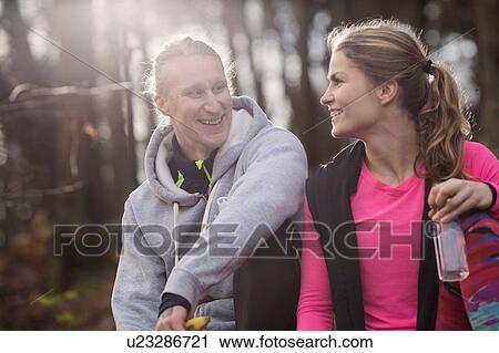 Stock Image - Couple wearing sports clothing holding water bottle sitting face to face smiling. Fotosearch