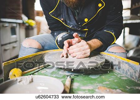Stock Image - Cropped front view of mid adult man shaping clay on pottery wheel. Fotosearch