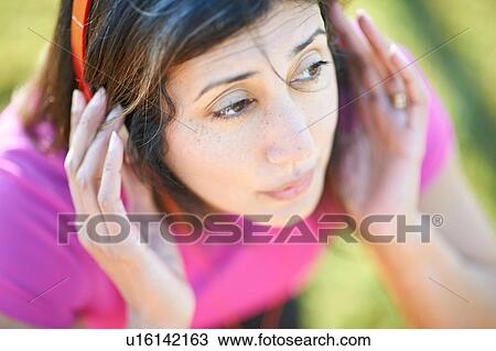 Stock Image - Cropped high angle view of mature woman wearing headphones, hands on ears looking away. Fotosearch
