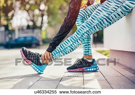Stock Photography - Cropped shot of female runner stretching legs on sidewalk. Fotosearch