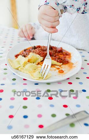 Stock Photo - Cropped shot of female toddler eating ravioli at table. Fotosearch