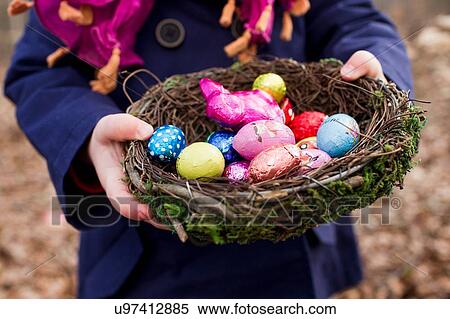 Stock Photography - Cropped shot of female toddler holding basket nest of easter eggs in forest. Fotosearch