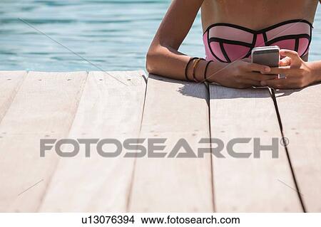 Picture - Cropped shot of girl in swimming pool using smartphone. Fotosearch
