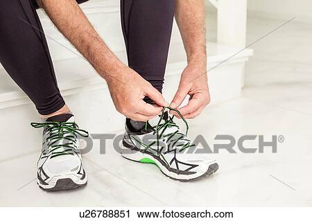 Stock Image - Cropped shot of senior mans hands tying trainer laces on staircase. Fotosearch