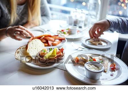 Stock Image - Cropped shot of young couples hands eating finger food in cafe. Fotosearch