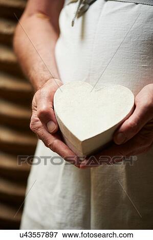 Stock Photo - Cropped view of person wearing apron holding heart shaped gift box. Fotosearch