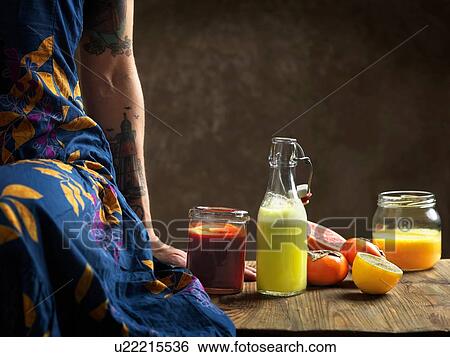 Cropped view of woman wearing dress sitting on table with raw juices in glass bottle and jars View Large Photo Image Stock Photograph - Cropped view of woman wearing dress sitting on table with raw juices in glass bottle and jars. Fotosearch