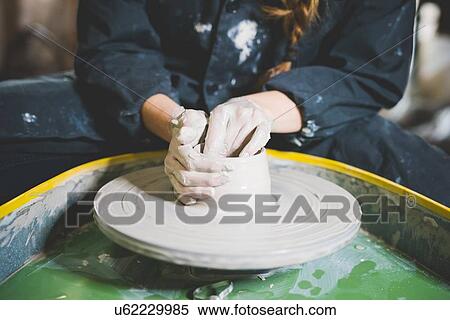 Stock Photography - Cropped view of young woman sitting at pottery wheel making clay pot. Fotosearch