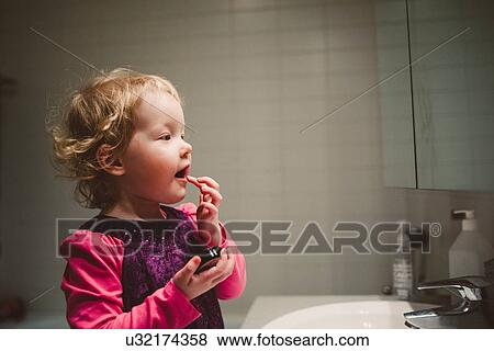 Cute girl looking in bathroom mirror applying lip gloss with finger View Large Photo Image Stock Photo - Cute girl looking in bathroom mirror applying lip gloss with finger. Fotosearch