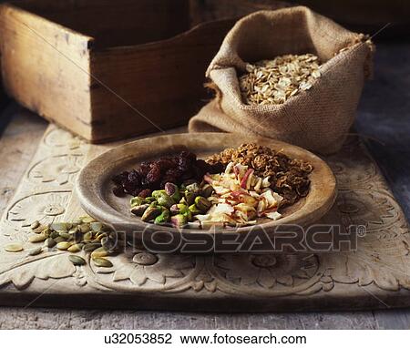 Stock Image - Dried fruits and nuts on wooden plate with burlap sack of oats. Fotosearch
