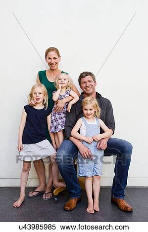 Stock Photography - Family portrait of parents and three young daughters in front of white wall. Fotosearch