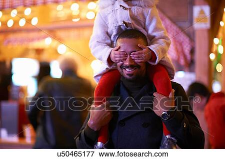 Stock Photo - Father carrying daughter on shoulders, daughter covering father's eyes. Fotosearch