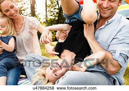 Stock Photo - Father turning daughter upside down at family picnic in park. Fotosearch
