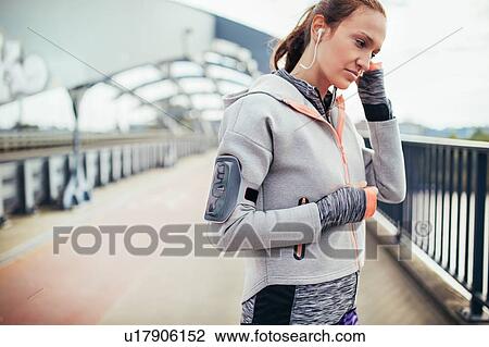 Stock Image - Female runner adjusting earphones on city footbridge. Fotosearch