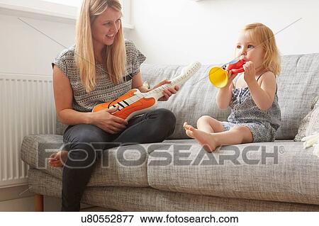 Female toddler and mother playing with toy trumpet and guitar on sofa View Large Photo Image Stock Photo - Female toddler and mother playing with toy trumpet and guitar on sofa. Fotosearch