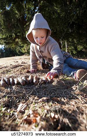 Stock Image - Female toddler playing with pine cones in forest. Fotosearch