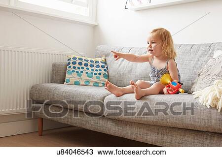 Stock Image - Female toddler playing with toy trumpet on sofa. Fotosearch