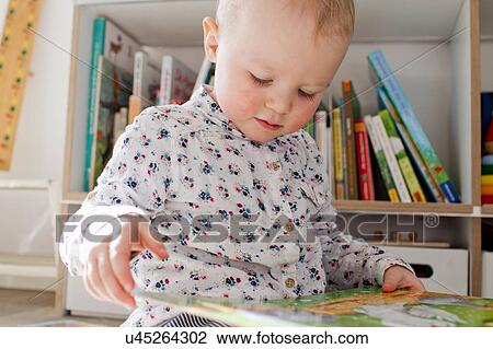 Stock Image - Female toddler reading book in playroom. Fotosearch