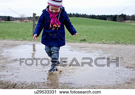 Stock Image - Female toddler wearing rubber boots splashing in puddle. Fotosearch