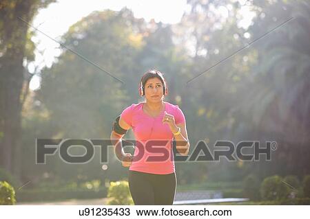 Front view of mature woman wearing headphones and armband jogging in park View Large Photo Image Stock Image - Front view of mature woman wearing headphones and armband jogging in park. Fotosearch