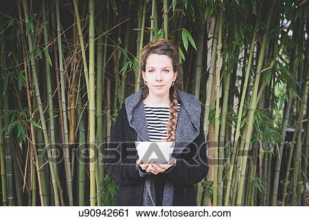 Front view of young woman standing in front of bamboo grove holding ceramic dish looking at camera View Large Photo Image Stock Image - Front view of young woman standing in front of bamboo grove holding ceramic dish looking at camera. Fotosearch