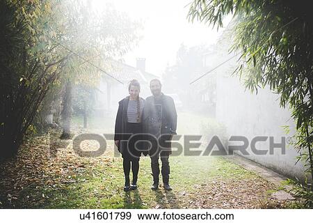 Full length front view of couple standing in misty garden looking at camera smiling View Large Photo Image Stock Photo - Full length front view of couple standing in misty garden looking at camera smiling. Fotosearch