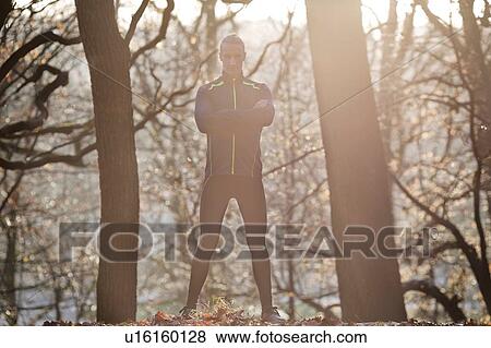 Stock Photo - Full length front view of mid adult man standing in forest arms folded looking at camera smiling. Fotosearch