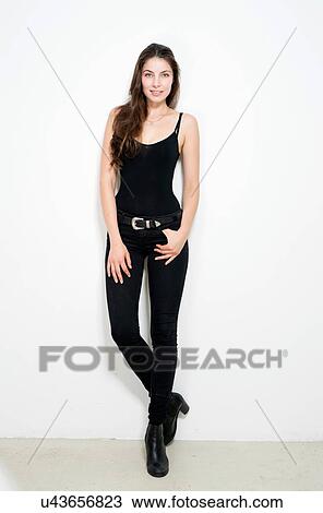Full length front view of young woman leaning against wall looking at camera smiling View Large Photo Image Stock Image - Full length front view of young woman leaning against wall looking at camera smiling. Fotosearch