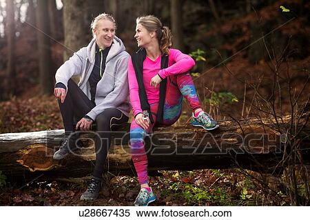 Stock Photography - Full length view of couple wearing sports clothing sitting on fallen tree, smiling. Fotosearch