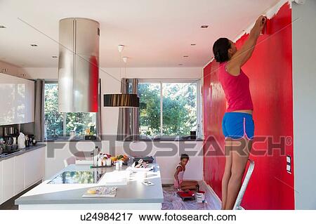Stock Photo - Girl and mother painting kitchen wall red with paint rollers. Fotosearch