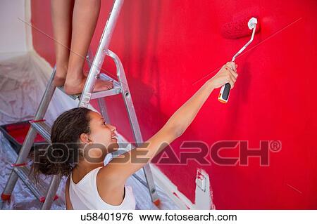 Stock Photograph - Girl and mother painting red wall with paint roller. Fotosearch
